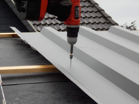 Professionele installatie van een lichtgrijze damwandplaat op een dak met een accuschroevendraaier